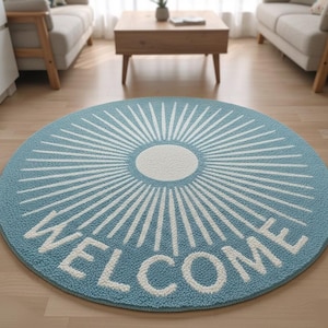 May include: A circular rug in light blue, featuring a white sunburst pattern and the word "WELCOME" in white. The rug is made of a soft, textured material, suitable for indoor use.