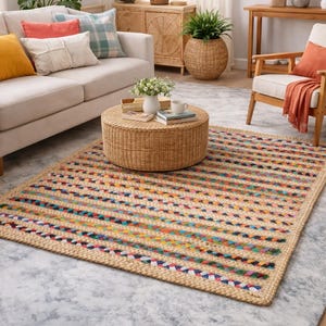 Peut inclure: Un tapis rectangulaire avec un motif tissé. Le tapis présente un fond beige naturel avec des rayures horizontales colorées bleues, vertes, rouges et jaunes. Le tapis est posé sur un sol gris clair.