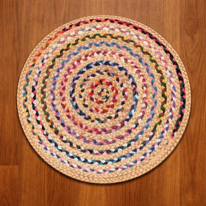 Könnte beinhalten: Ein runder geflochtener Teppich mit Spiralmuster. Der Teppich hat einen natürlichen beigefarbenen Farbton mit farbenfrohen Akzenten in Rot, Blau, Gelb und Grün. Der Teppich besteht aus gewebtem Material und ist für den Innenbereich geeignet.