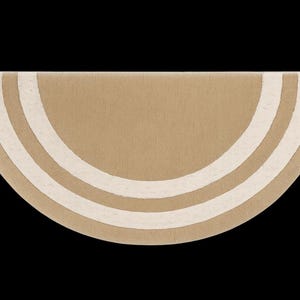 May include: A half-circle rug in a neutral tan color with three off-white curved stripes. The rug has a soft, textured appearance and is set against a black background. The design is simple and modern.