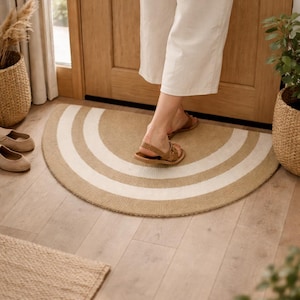 May include: A half-circle beige and white striped doormat. The mat is placed in front of a wooden door. Woven baskets with plants and shoes are visible in the background.
