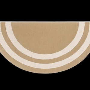 May include: A half-circle rug in a neutral tan color with three off-white curved stripes. The rug has a soft, textured appearance and is set against a black background. The design is simple and modern.