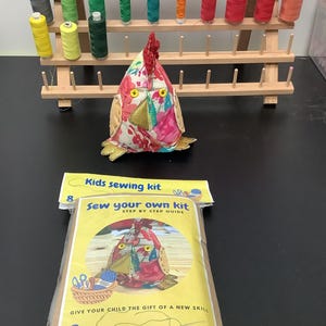 May include: A kids' sewing kit with a colorful chicken-shaped project and a wooden thread rack filled with spools of thread. The kit includes a "Sew Your Own Kit" step-by-step guide and is recommended for ages 8 and up.