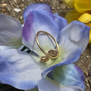 May include: A gold-colored ring with a double spiral design. The ring is on a blue and purple fabric background.
