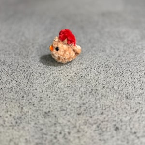 May include: A small, plush, light brown chick with a red crest and an orange beak. The handmade chick is a soft, textured toy, perfect for Easter or as a decorative item. The chick is a cute, whimsical design.
