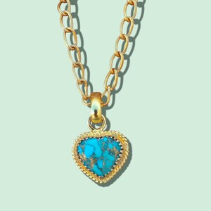 Peut inclure: Un collier doré avec un pendentif en forme de cœur. Le pendentif présente une pierre turquoise avec des éclats dorés, encadrée par une bordure dorée texturée. La chaîne est composée de maillons ovales.