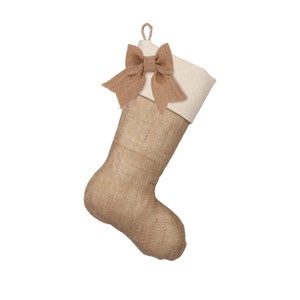 May include: A burlap Christmas stocking with a white cuff and a brown burlap bow.