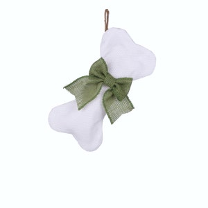 May include: White fabric dog bone ornament with a green burlap bow. The bone shape has a textured appearance and is suspended by a brown string. A decorative item for pet lovers.