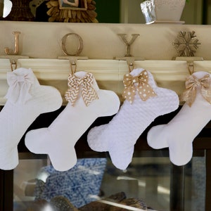 May include: Four white bone-shaped Christmas stockings, each with a decorative bow. The bows have different patterns, including plain, polka dots, and chevron. The word "JOY" is displayed above the stockings.