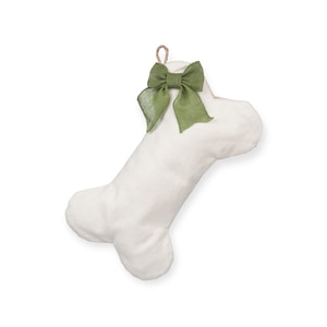 May include: A white, bone-shaped dog toy with a green bow at the top. The toy is made of a textured fabric and has a loop for hanging. A charming pet accessory.