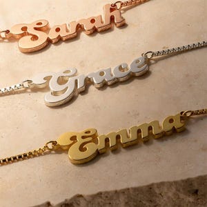 Könnte beinhalten: Drei Namensketten in Roségold, Silber und Gold. Die Namen "Sarah", "Grace" und "Emma" sind in einer Schreibschrift dargestellt. Jede Halskette befindet sich an einer filigranen Kette, ideal für personalisierten Schmuck.
