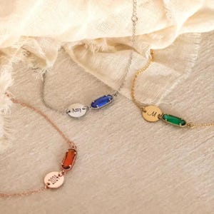 Könnte beinhalten: Drei zarte Armbänder mit personalisierten Details. Eines ist roségoldfarben mit einem orangefarbenen Edelstein und der eingravierten Jahreszahl "2024". Ein weiteres ist silberfarben mit einem blauen Edelstein und dem Namen "Amy". Das dritte ist goldfarben mit einem grünen Edelstein und dem Buchstaben "M".