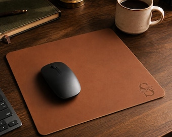 May include: A square brown leather mouse pad with rounded corners, featuring a black wireless computer mouse placed on its surface. The bottom right corner of the mouse pad is engraved with a large letter S and the name SCOTT centered inside.