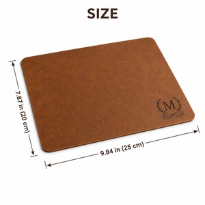 May include: A rectangular brown mouse pad with rounded corners, featuring a laser-engraved laurel wreath, the letter M, and the name MORGAN. The dimensions are 7.87 inches by 9.84 inches, as indicated by the measurement lines on the image.