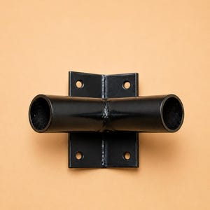 May include: A black metal pipe fitting with two horizontal openings and a right-angle bracket. The bracket has four holes for mounting. The object is set against a light orange background.