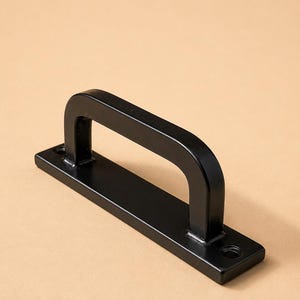 May include: A black metal pull handle with a rectangular base and a curved handle. The handle has a smooth, glossy finish and is designed for easy gripping. The base features two holes for mounting. The handle is approximately 6 inches long.