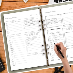 Könnte beinhalten: ADHS-Tagesplaner mit Abschnitten für Aufgaben, Zeit und Stimmung. Enthält eine Routine-Checkliste und Platz für ein Brainstorming. Der Planer ist geöffnet, mit einer Hand, die einen Stift hält.