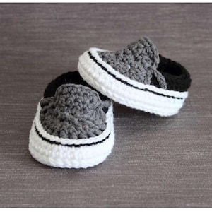 May include: A pair of handmade crochet baby shoes. The shoes are gray and black with white soles and a black stripe. The shoes are designed to look like miniature sneakers.