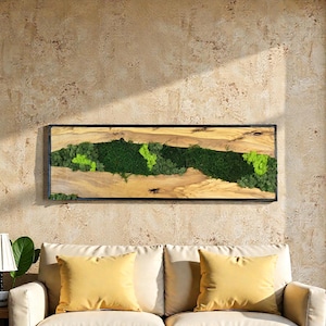 May include: A rectangular wooden wall art piece with a black frame. The art features a natural wood grain background with a central strip of green moss and lighter green accents. The piece is mounted on a textured beige wall.