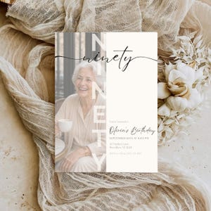 Op de afbeelding: Een rechthoekige verjaardagsuitnodigingskaart met een zwart-witfoto van een ouder persoon die een kopje vasthoudt. De tekst luidt NINETY, You're invited to Olivia's Birthday, SEPTEMBER 16TH AT 8:00 PM, 42 Market Lane, Brooklyn, NY 11201, RSVP to Olivia (555) 123-4567.