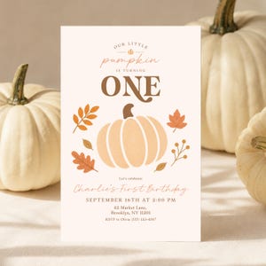 Op de afbeelding: Een rechthoekige verjaardagsuitnodiging met een crèmekleurige achtergrond en een centrale illustratie van een lichtoranje pompoen omringd door herfstbladeren. De tekst luidt: Our little pumpkin is turning ONE, Charlie's First Birthday, September 16th at 2:00 PM, 42 Market Lane, Brooklyn, NY 11201, RSVP to Olivia (555) 123-4567.
