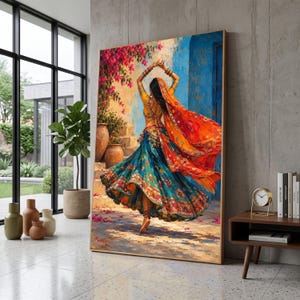 May include: A vertical wall art print depicting a person dancing in a vibrant, multi-colored traditional outfit with a flowing teal skirt and orange dupatta. The scene features a blue wall, pink bougainvillea flowers, and terracotta pots.