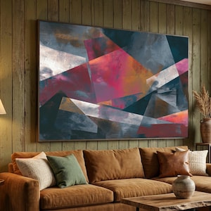Pode incluir: Grande pintura abstrata emoldurada com formas geométricas em vermelho, rosa, azul, cinza e branco. A obra de arte está pendurada acima de um sofá marrom com almofadas. O quarto tem uma atmosfera rústica e acolhedora.