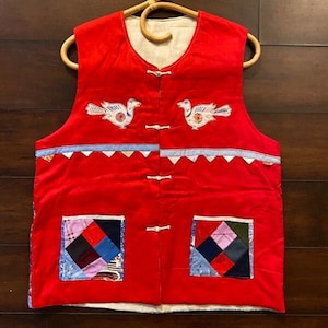 May include: Red quilted vest with two embroidered birds and two patch pockets. The vest has a white lining and a button closure.