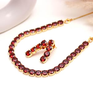 Puede incluir: Un collar de tono dorado y un par de pendientes a juego, cada uno con una hilera continua de piedras redondas de color rojo intenso facetadas y engastadas en metal. El collar incluye una cadena fina dorada con un cierre de mosquetón.