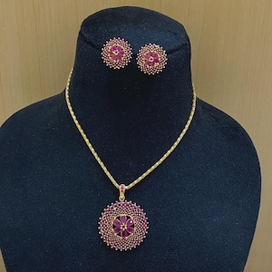 Pu&ograve; includere: Un set di collana e orecchini color oro con pendenti circolari. Ogni pezzo &egrave; decorato con un motivo floreale centrale composto da pietre rosa a forma di goccia, circondato da un bordo denso di piccoli cristalli rosa scintillanti.