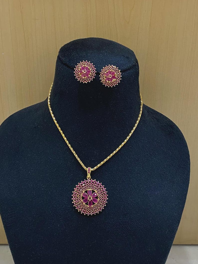 Pu&ograve; includere: Un set di collana e orecchini color oro con pendenti circolari. Ogni pezzo &egrave; decorato con un motivo floreale centrale composto da pietre rosa a forma di goccia, circondato da un bordo denso di piccoli cristalli rosa scintillanti.