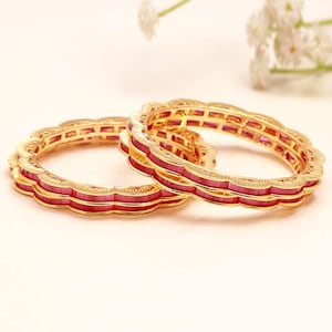 Può includere: Due bracciali circolari in oro con un design a bordo smerlato. Ogni bracciale è intarsiato con una fila continua di pietre rettangolari di un vibrante rosso rosato, incastonate nella struttura metallica con un motivo strutturato e ripetitivo.