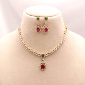 Puede incluir: Un conjunto de collar y pendientes en tono dorado con eslabones circulares incrustados con piedras claras. El collar tiene un colgante central con una piedra verde en forma de lágrima sobre una piedra roja más grande.