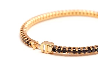 May include: Gold-coloured bracelet with a line of small, black gemstones. The bracelet has a hinged clasp. The design is simple and elegant, suitable for everyday wear or special occasions.