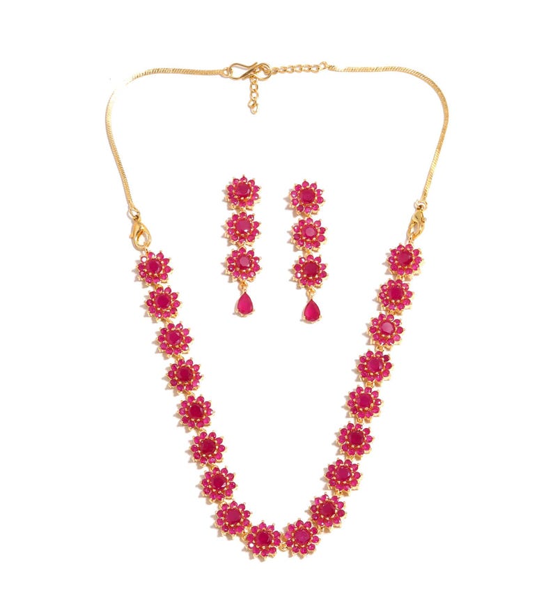 May include: A gold necklace and earring set with ruby-red floral designs. The necklace and earrings have a fine chain and are decorated with bright red gemstones. The earrings feature a teardrop-shaped gemstone at the bottom.