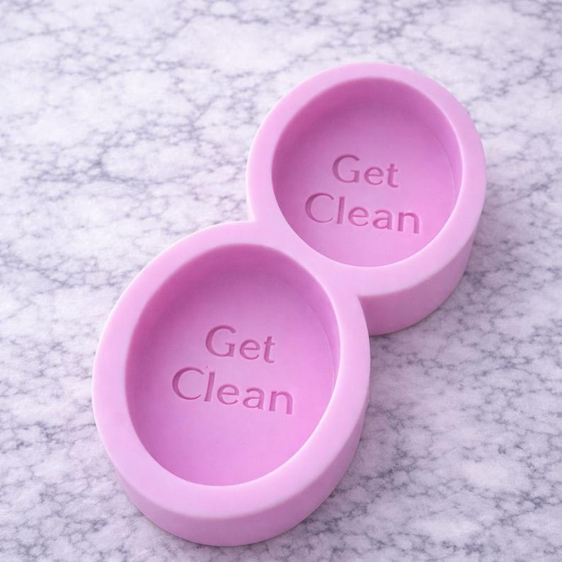 Puede incluir: Un molde de silicona de color lila con dos cavidades ovaladas conectadas. Cada cavidad tiene las palabras "Get Clean" en relieve en el centro. El molde est&aacute; dise&ntilde;ado para hacer jab&oacute;n o manualidades similares.