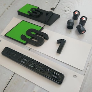 May include: Black and green S1 and Quattro emblems, along with black tire valve stem caps with red accents. The S1 emblems have a green background. The number 1 is also included.