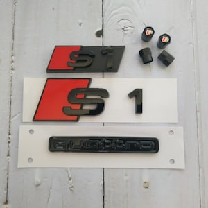 May include: A collection of black and red car badges and valve stem caps. The badges feature the letters "S1" and the word "quattro". The valve caps have a red and white logo.