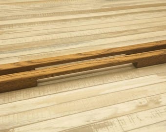 May include: Two long, rectangular wooden cabinet handles with a natural brown oak grain finish. Each handle features a smooth, linear design with a recessed grip section running along the centre, showcasing the distinct texture of the wood grain.