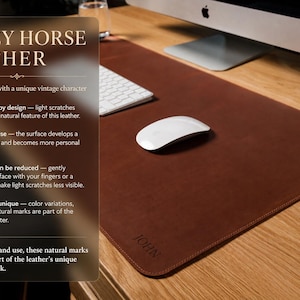 May include: A rectangular brown leather desk mat with rounded corners and the name JOHN embossed in the bottom corner. The mat features a smooth surface texture and is displayed on a wooden desk with a white computer mouse and keyboard.