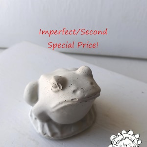 May include: A small, white, concrete frog figurine. The frog is sitting on a base and has a textured surface. The image text reads "Imperfect/Second Special Price!" and "100% Handmade by Wire Animals CA. USA".