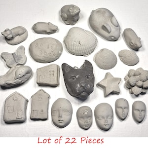 May include: A collection of 22 small, gray concrete figurines. The assortment includes animal shapes like a frog, mouse, and cat, along with a butterfly, houses, faces, and a star. The text "Lot of 22 Pieces" is visible at the bottom.