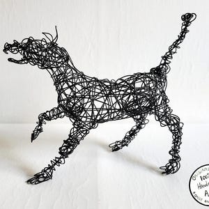 May include: A black wire sculpture of a dog in a running pose. The sculpture is made of intertwined wire, creating a three-dimensional form. The dog's features, including its head, legs, and tail, are clearly defined. The sculpture is on a white background.