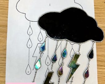 May include: A stained glass storm cloud pattern with raindrops and lightning bolts hanging from it. The pattern is numbered 1 through 8. The text "Storm Cloud" and "Pattern by Weld and Whimsy Glass Studio" is at the top of the page. The text "Hobby & Commercial License" is at the bottom of the page.