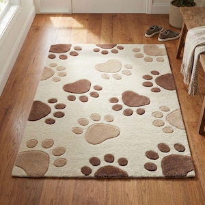 Pode incluir: Um tapete retangular com um padrão repetitivo de pegadas de patas em vários tons de castanho e bege sobre um fundo creme. O tapete tem um pelo macio e texturizado e está colocado sobre um chão de madeira num ambiente interior.