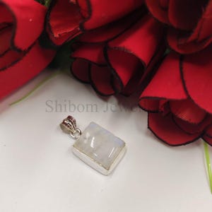 May include: A rectangular moonstone pendant set in a silver bezel with a silver bail. The stone has a translucent, milky white appearance with subtle blue iridescence. The text Shibom Jewelers is visible in the background behind the pendant.