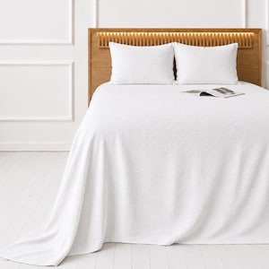 May include: A bed with a light wood headboard and white bedding. Two white pillows rest against the headboard. A white textured blanket covers the bed. A magazine lies on top of the blanket.