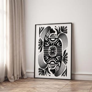May include: Black and white framed art print featuring a symmetrical design. The artwork showcases a central geometric shape with floral and abstract elements. The print is displayed on a wooden floor, leaning against a white wall.