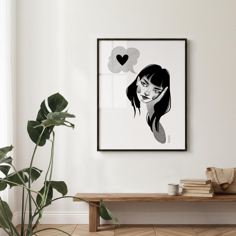 May include: Black and white framed art print featuring a stylized illustration of a woman with a thought bubble containing a heart. The artwork is displayed on a white wall above a wooden bench with a plant and other decorative items.