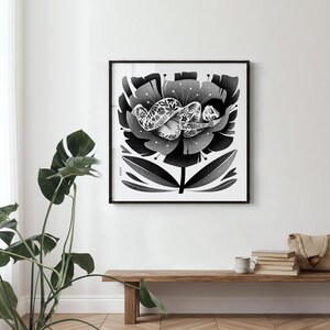 May include: Black and white art print in a black frame. The artwork depicts a person lying in a large flower. The person has detailed floral tattoos. The flower and person are in shades of gray. The print is displayed on a white wall.